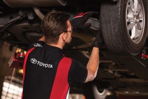 Man working under car in a licensed Toyota long sleeve automotive dealership uniform